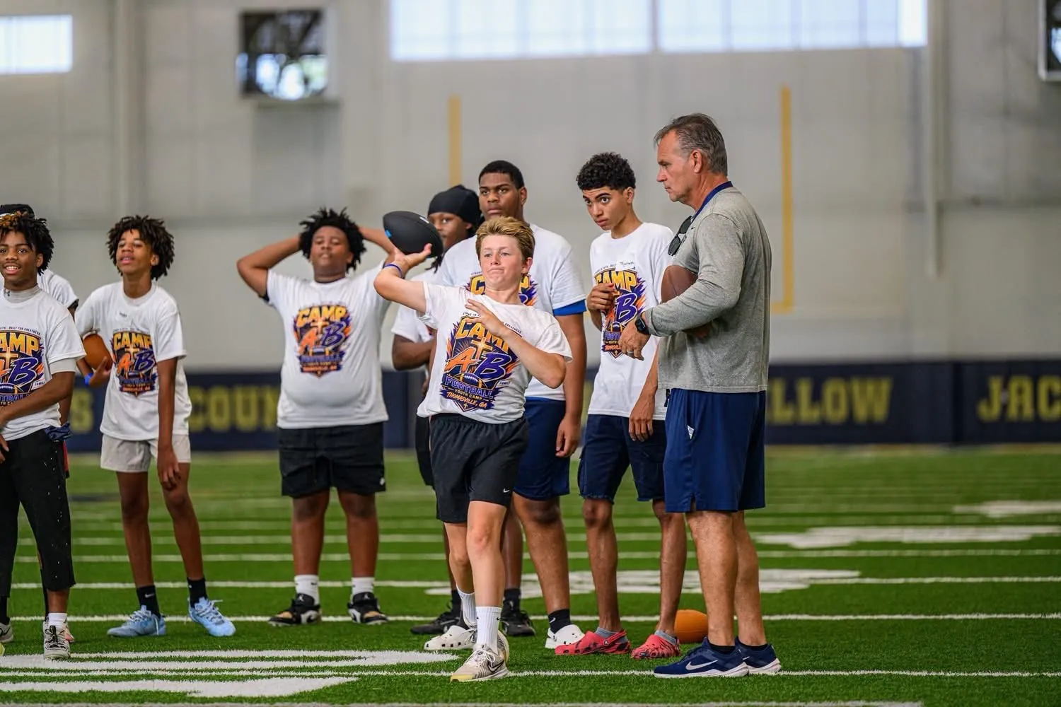 Young athletes practicing a football throw with a coach at Camp AB