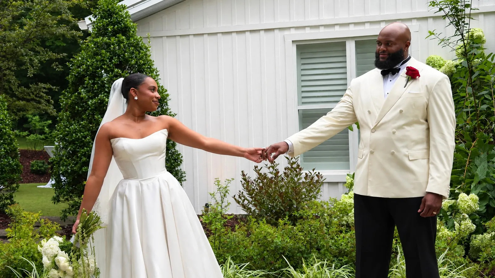 Austin and his wife in a posed wedding portrait in a garden in front of a board-and-batten building