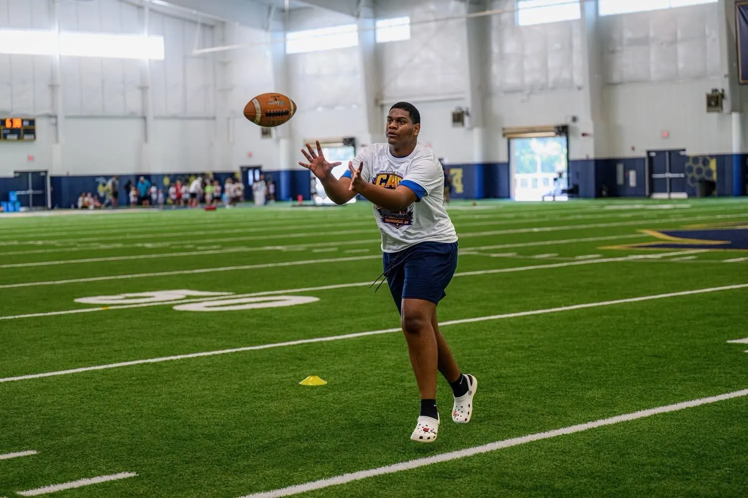 A Camp AB participant reaching to catch a football on the indoor field